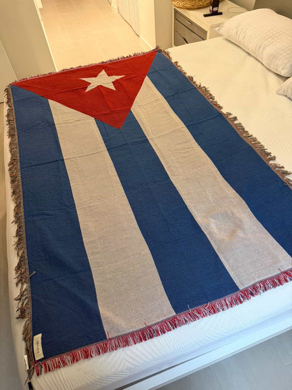 Cuban flag-patterned blanket draped over a bed in a bedroom setting.