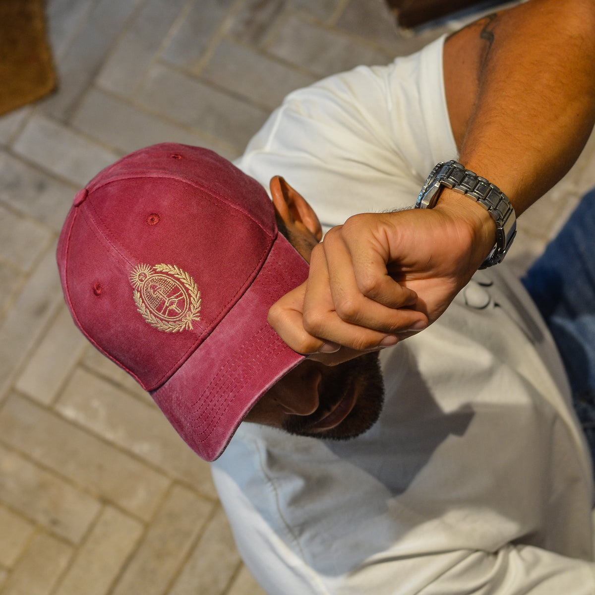 A person wearing a faded maroon baseball cap with a gold embroidered emblem, shown from an overhead angle in an indoor setting with stone tile flooring.