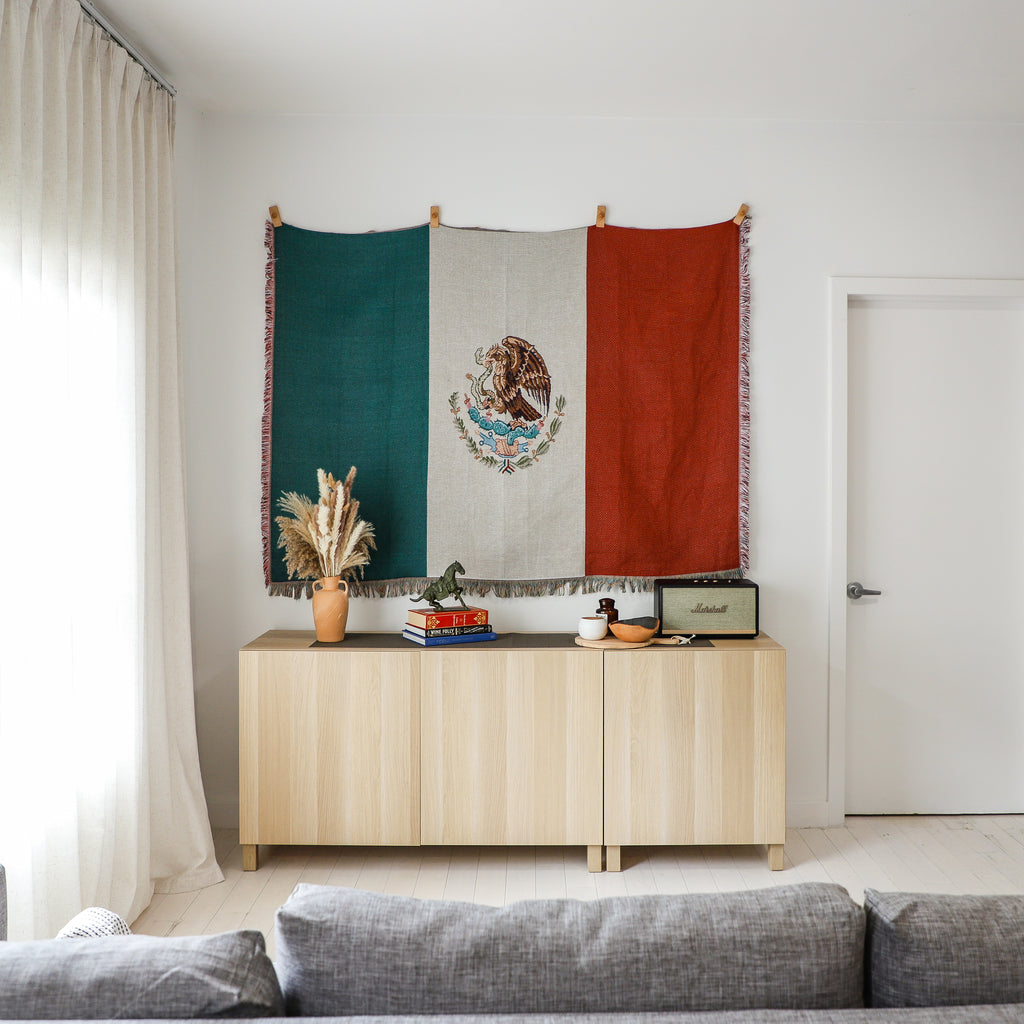 Living room with a wooden sideboard, Mexican flag tapestry, and gray sofa.