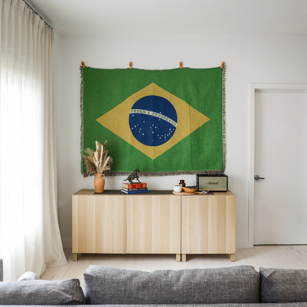 Living room with a Brazilian flag tapestry on the wall above a wooden cabinet.