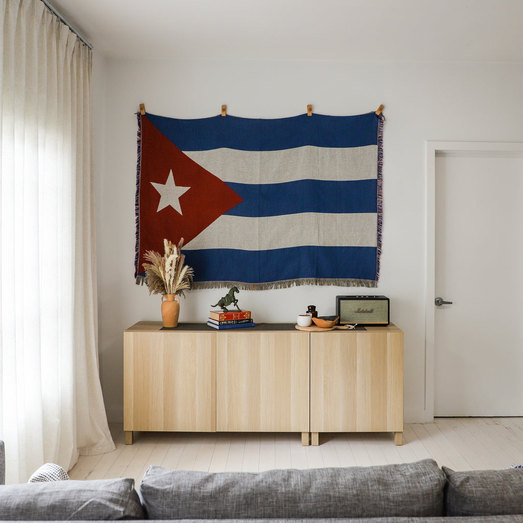 Cuban flag tapestry hanging above a wooden cabinet in a living room.