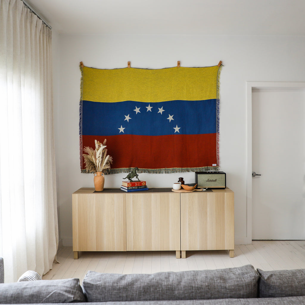 Living room with a wooden cabinet, decorative items, and a Venezuelan flag tapestry.