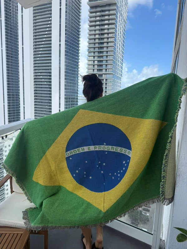 Person holding a Brazilian flag on a balcony with tall buildings in the background