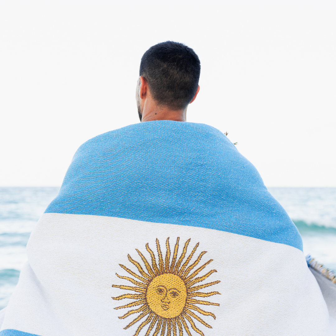 Man by the sea wrapped in the Argentina flag woven throw blanket