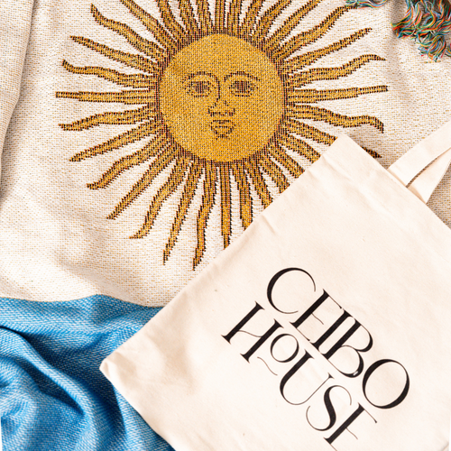 Sun of May detail on the Argentina flag woven throw blanket next to a Ceibo House tote bag