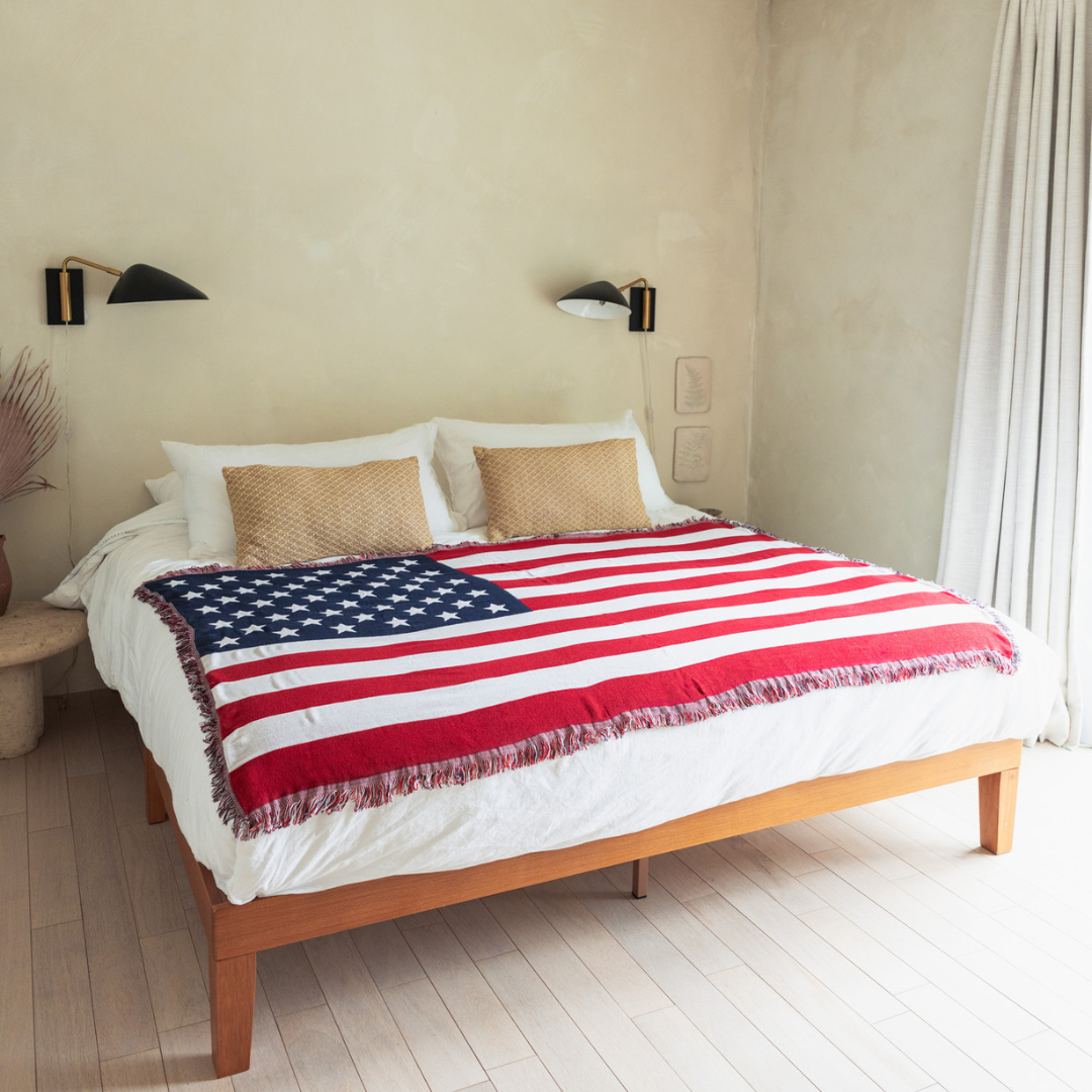 American flag woven throw blanket spread across a bed in a bright bedroom