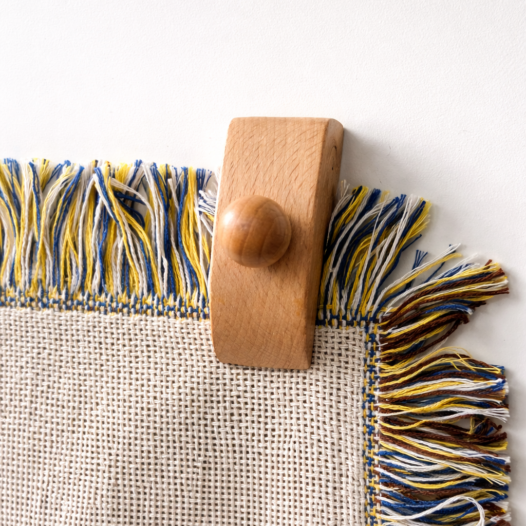 Wooden blanket hanger clip holding the fringed edge of a woven throw